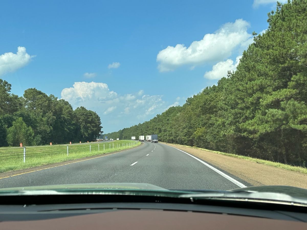 Looking forward out of a car, freeway ahead, green grass, blue sky.