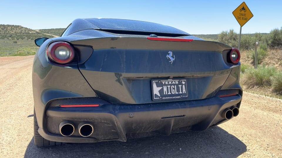 Ferrari sports car parked on a remote, gravel road next to a signing cautioning drivers to share the road with ATVs